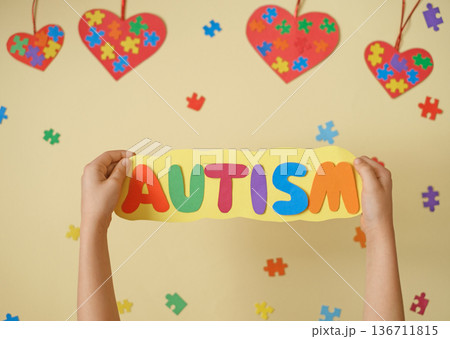 The word Autism is made of paper on a card in the hands of a child. A poster as a sign of support for people with autism spectrum disorder. The word Autism is made of paper on a card in the hands of a child. A poster as a sign of support for people with autism spectrum disorder. 136711815