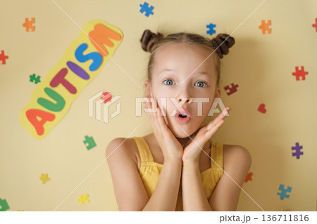 Portrait of surprised young girl with colorful Autism sign and puzzle pieces on yellow background. Concept of autism awareness, neurodiversity acceptance, inclusive education and child support Portrait of surprised young girl with colorful Autism sign and puzzle pieces on yellow background. Concept of autism awareness, neurodiversity acceptance, inclusive education and child support 136711816