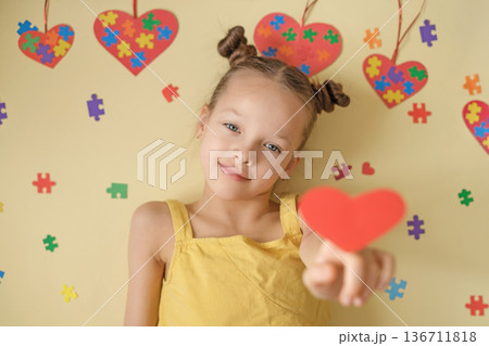 A sweet, kind little girl shows a red heart, showing support for autistic unique people.  World Autism Awareness Day 136711818