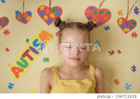 A beautiful peaceful girl with her eyes closed in the process of thinking on a background decorated with puzzles and hearts. The complexity and variety of manifestations of Autism. A beautiful peaceful girl with her eyes closed in the process of thinking on a background decorated with puzzles and hearts. The complexity and variety of manifestations of Autism. 136711819