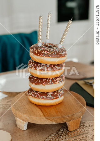 Stacked donuts with candles on wooden stand. Festive dessert concept ideal for birthday celebrations, party marketing, bakery promotion and sweet lifestyle themes. 136711976