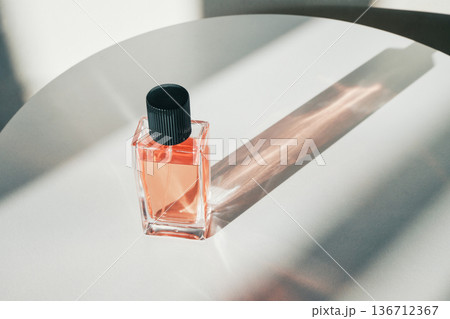 Bottle of cologne reflecting sunlight and creating shadow on bright surface Bottle of cologne reflecting sunlight and creating shadow on bright surface 136712367