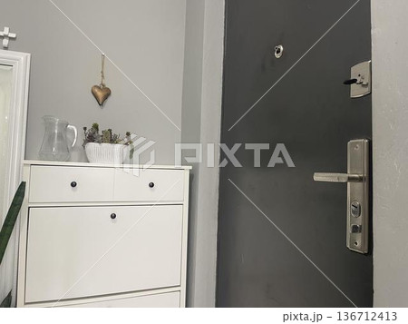 A white cabinet with a jar and a plant near the door A white cabinet with a jar and a plant near the door 136712413
