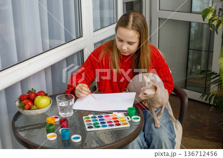 Concentrated child girl painting and sitting with cat pet on the terrace.  136712456