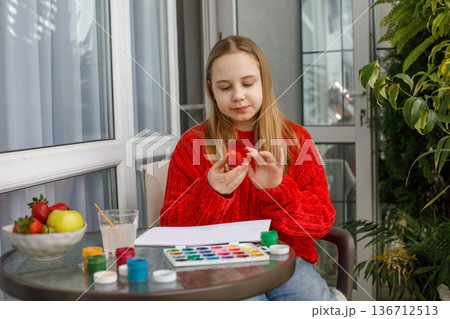 Cheerful young girl eating red strawberry and sitting on a balcony. Preteen child, leisure activity Cheerful young girl eating red strawberry and sitting on a balcony. Preteen child, leisure activity 136712513