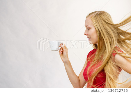 Blonde girl blowing hair holds coffee cup 136712736