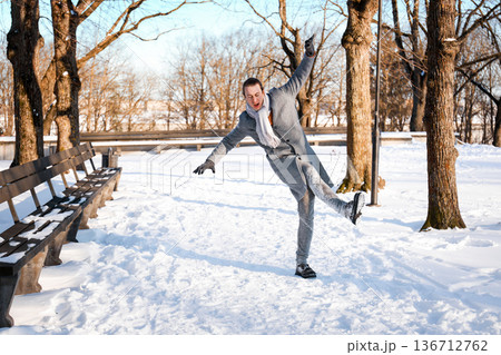 Man losing balance and slipping on an icy path in a snowy park. Winter accident concept showing the risk of falling, slippery footwear, and injury danger outdoors. High quality photo 136712762