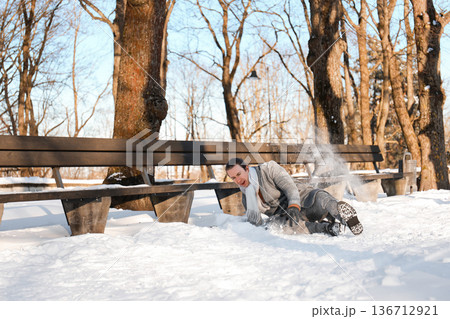Man slipping and falling on snow near a bench in a winter park. Young guy crashing down on slippery ice during a sunny cold day. Winter accident concept. High quality photo Man slipping and falling on snow near a bench in a winter park. Young guy crashing down on slippery ice during a sunny cold day. Winter accident concept. High quality photo 136712921