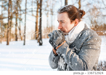 A man freezes in a winter park, warming his gloved hands with his breath. Concept of freezing and cold winter. High quality photo A man freezes in a winter park, warming his gloved hands with his breath. Concept of freezing and cold winter. High quality photo 136712924