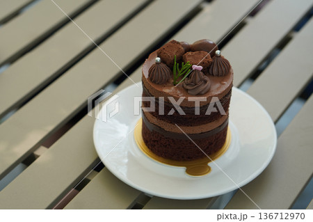 top view chocolate cake with layers of chocolate pudding and coffee pudding layers, decorated with chocolate ball, silver sprinkle and green grass, on a golden paper, are put on a white ceramic 136712970