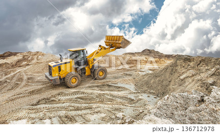 A large yellow loader moves earth and gravel at a construction site during the day, while clouds form in the sky. Heavy equipment leveling the construction site A large yellow loader moves earth and gravel at a construction site during the day, while clouds form in the sky. Heavy equipment leveling the construction site 136712978