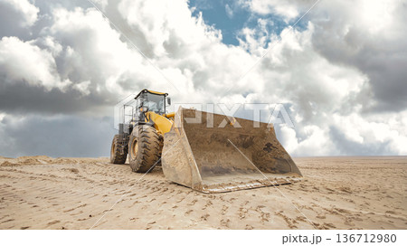 A bulldozer or loader moves across sandy terrain with a large dump ahead. Earthworks are being prepared for a construction project 136712980