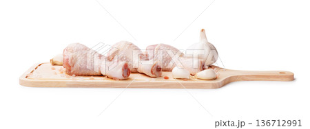 Raw chicken drumsticks on a wooden cutting board with garlic and pink salt. Fresh poultry meat preparation isolated on white background. Side view. High quality photo 136712991