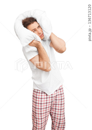 Annoyed man in pajamas covering his head with a white pillow to block noise, isolated on white background. Concept of insomnia, stress, headache, or loud neighbors preventing sleep. High quality photo Annoyed man in pajamas covering his head with a white pillow to block noise, isolated on white background. Concept of insomnia, stress, headache, or loud neighbors preventing sleep. High quality photo 136713120