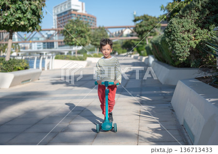Young Boy Riding A Scooter In A Sunny Abu Dhabi Park Area Young Boy Riding A Scooter In A Sunny Abu Dhabi Park Area 136713433