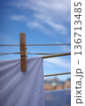 Wooden clothespin holding white laundry on clothesline against blue sky 136713485