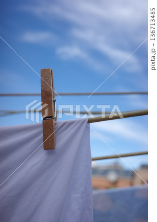 Wooden clothespin holding white laundry on clothesline against blue sky Wooden clothespin holding white laundry on clothesline against blue sky 136713485
