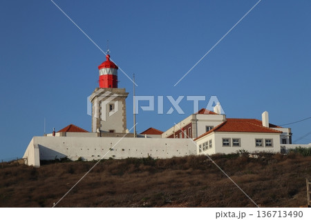 Red lighthouse tower and traditional white buildings at Cabo da Roca, Portugal. 136713490