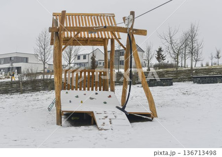 Snow-covered playground and snow-covered playhouse on the children's playground. Concept of winter and winter nature. Snow-covered playground and snow-covered playhouse on the children's playground. Concept of winter and winter nature. 136713498