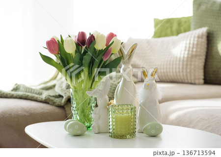 Living Room Decorated Easter Eggs with Bunny Figurines, Candles and Tulips. Cozy Spring Holiday Arrangement Living Room Decorated Easter Eggs with Bunny Figurines, Candles and Tulips. Cozy Spring Holiday Arrangement 136713594