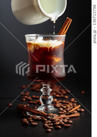 Cream is poured into a glass with black coffee and ice. Cream is poured into a glass with black coffee and ice. 136713798