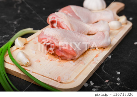 Raw chicken drumsticks on a wooden board with garlic, green onions, and pink salt on a dark marble background prepared for cooking. High quality photo Raw chicken drumsticks on a wooden board with garlic, green onions, and pink salt on a dark marble background prepared for cooking. High quality photo 136715326