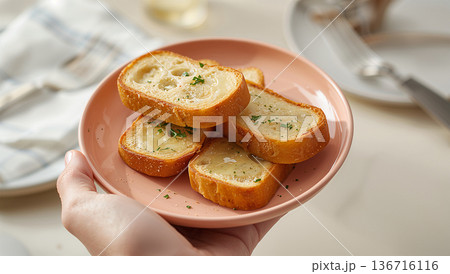 日本人の手が皿を支えガーリックトーストを配膳する温かな食卓 日本人の手が皿を支えガーリックトーストを配膳する温かな食卓 136716116