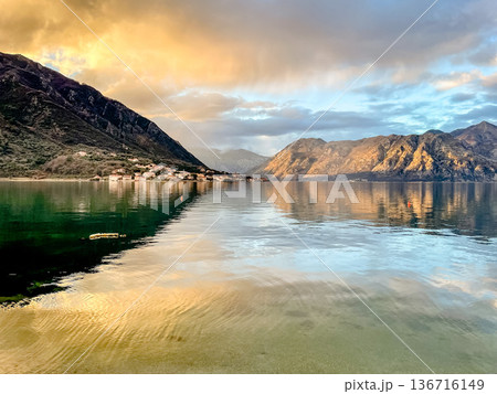 Tranquil shoreline showcasing golden sunlight and distant peaks Tranquil shoreline showcasing golden sunlight and distant peaks 136716149