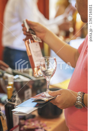 Man holding wine glass and bottle of rose wine during tasting event, rose wine at festival stand. Concept of wine tasting, rose wine promotion, beverage marketing event Man holding wine glass and bottle of rose wine during tasting event, rose wine at festival stand. Concept of wine tasting, rose wine promotion, beverage marketing event 136716881