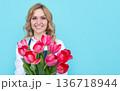 smiling girl in apron with spring tulip flowers on blue background 136718944