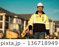 Caucasian man, construction worker in helmet at construction site. Industry engineer worker in hardhat near bulldozer or digger tractor. Concept of construction industry. Construction site manager. 136718949