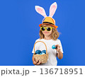 Funny easter child. Portrait of child with bunny ears hold easter basket with easter eggs, isolated on studio background. Funny easter bunny with rabbit ears. 136718951