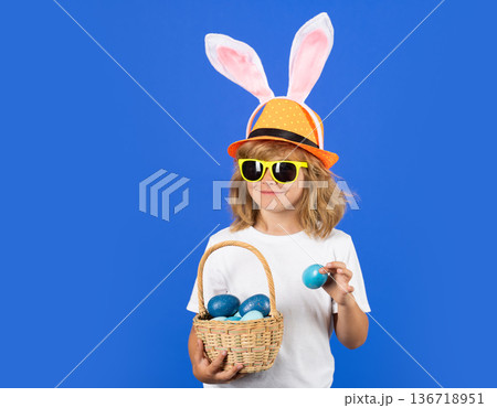 Funny easter child. Portrait of child with bunny ears hold easter basket with easter eggs, isolated on studio background. Funny easter bunny with rabbit ears. 136718951