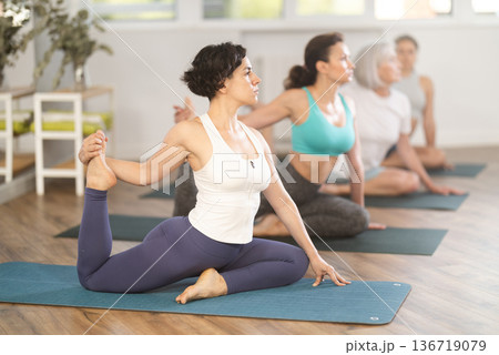 Woman performing Eka Pada Kapotasana during group yoga session Woman performing Eka Pada Kapotasana during group yoga session 136719079