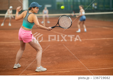 Young female tennis player engrossed in doubles on clay court 136719082