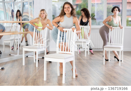 Young woman stands next to chair, leans on back and performs set of lap dance movements Young woman stands next to chair, leans on back and performs set of lap dance movements 136719166