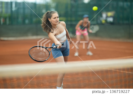 Fit girl engrossed in doubles tennis game on clay court Fit girl engrossed in doubles tennis game on clay court 136719227