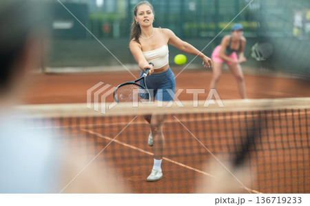Two young women playing doubles tennis Two young women playing doubles tennis 136719233