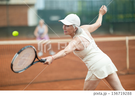 Aged woman playing friendly tennis match outdoors Aged woman playing friendly tennis match outdoors 136719288