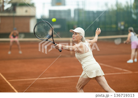 Two elderly women playing tennis against young women 136719313