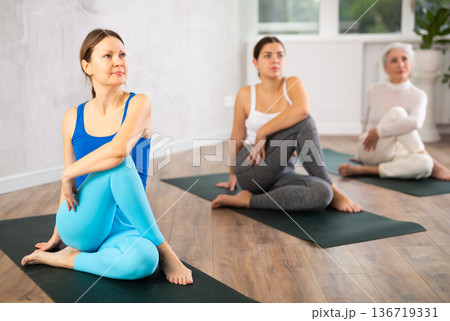 Concentration girl maintaining mental and physical health attending group yoga class at modern studio, practicing twisting poses Concentration girl maintaining mental and physical health attending group yoga class at modern studio, practicing twisting poses 136719331