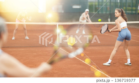 Young female tennis player engrossed in doubles on clay court 136719377