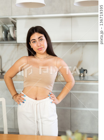 Smiling young woman posing against background of white kitchen Smiling young woman posing against background of white kitchen 136719395