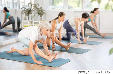Woman standing yoga pose and making full body stretching workout with group in room 136719435
