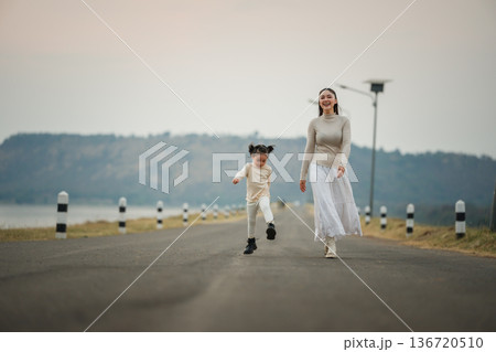 Mother and child girl walking and playing on a scenic road during dusk near river 136720510