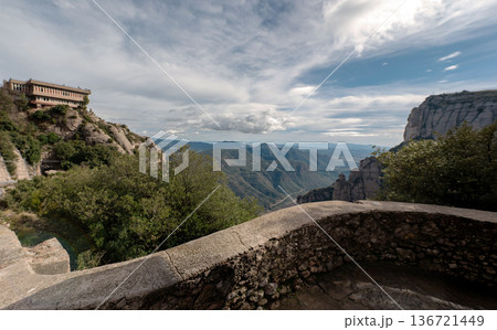 panoramic view from a stone lookout point at Montserrat, Spain. Featuring rugged mountains, a building on a cliff, and a vast valley under a cloudy blue sky. panoramic view from a stone lookout point at Montserrat, Spain. Featuring rugged mountains, a building on a cliff, and a vast valley under a cloudy blue sky. 136721449