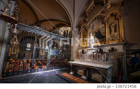 Interior view of Montserrat Monastery in Spain, featuring an ornate iron gate, religious paintings, and a grand organ pipe system under a vaulted ceiling Interior view of Montserrat Monastery in Spain, featuring an ornate iron gate, religious paintings, and a grand organ pipe system under a vaulted ceiling 136721456