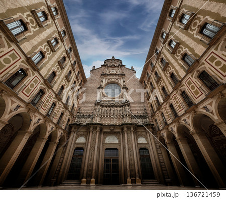 Low angle view of the ornate facade and courtyard of Montserrat Monastery in Catalonia, Spain, under a blue sky. Historic landmark and spiritual pilgrimage site near Barcelona 136721459