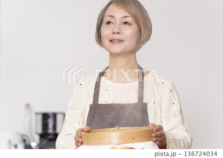 キッチンでさつま芋の蒸しパンをせいろで蒸して作るシニア女性 キッチンでさつま芋の蒸しパンをせいろで蒸して作るシニア女性 136724034