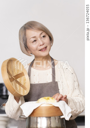 キッチンでさつま芋の蒸しパンをせいろで蒸して作るシニア女性 キッチンでさつま芋の蒸しパンをせいろで蒸して作るシニア女性 136724055